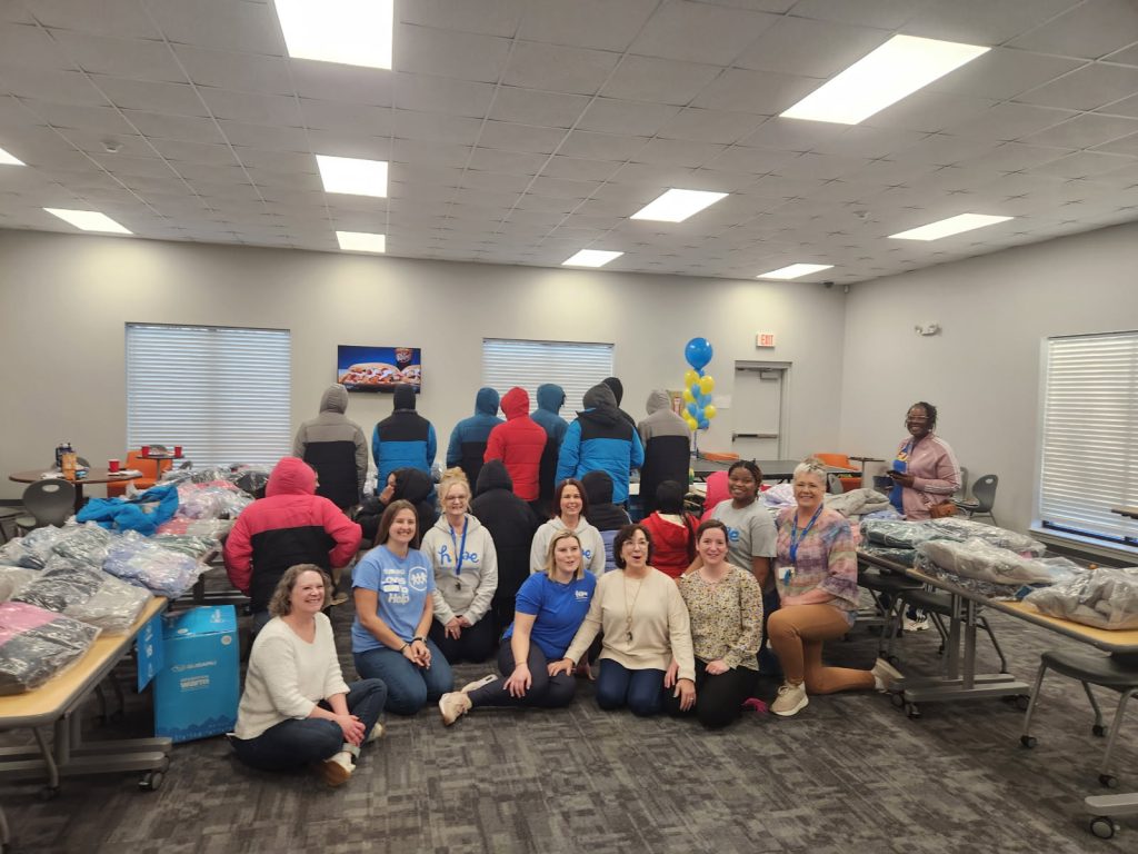 Staff from Subaru of Spartanburg kneel and pose for a picture in front of children showcasing their new coats for Operation Warm, a donation drive to give coats to needy children.