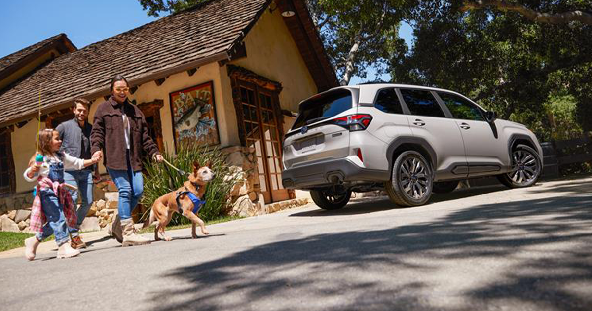 A family walking their dog across the street from their home with a Subaru Forester parked in the driveway