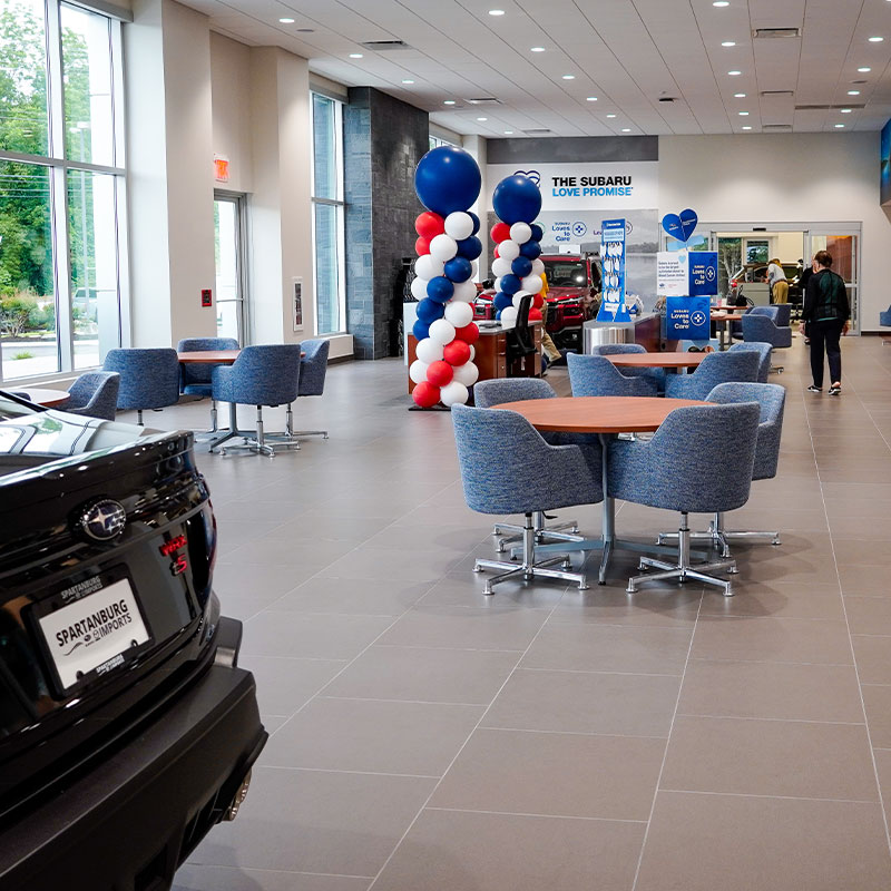 The lobby of Subaru of Spartanburg is pictured, showcasing tables and chairs, new Subarus, and a welcoming atmosphere
